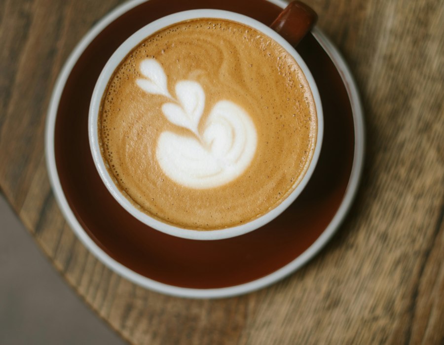 木のテーブルに置かれたラテアートのカフェラテ